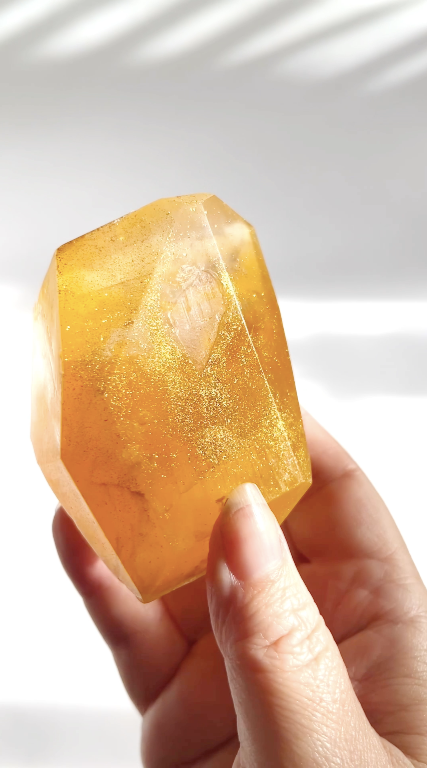 Hand holding a large orange gem shaped soap against a white background