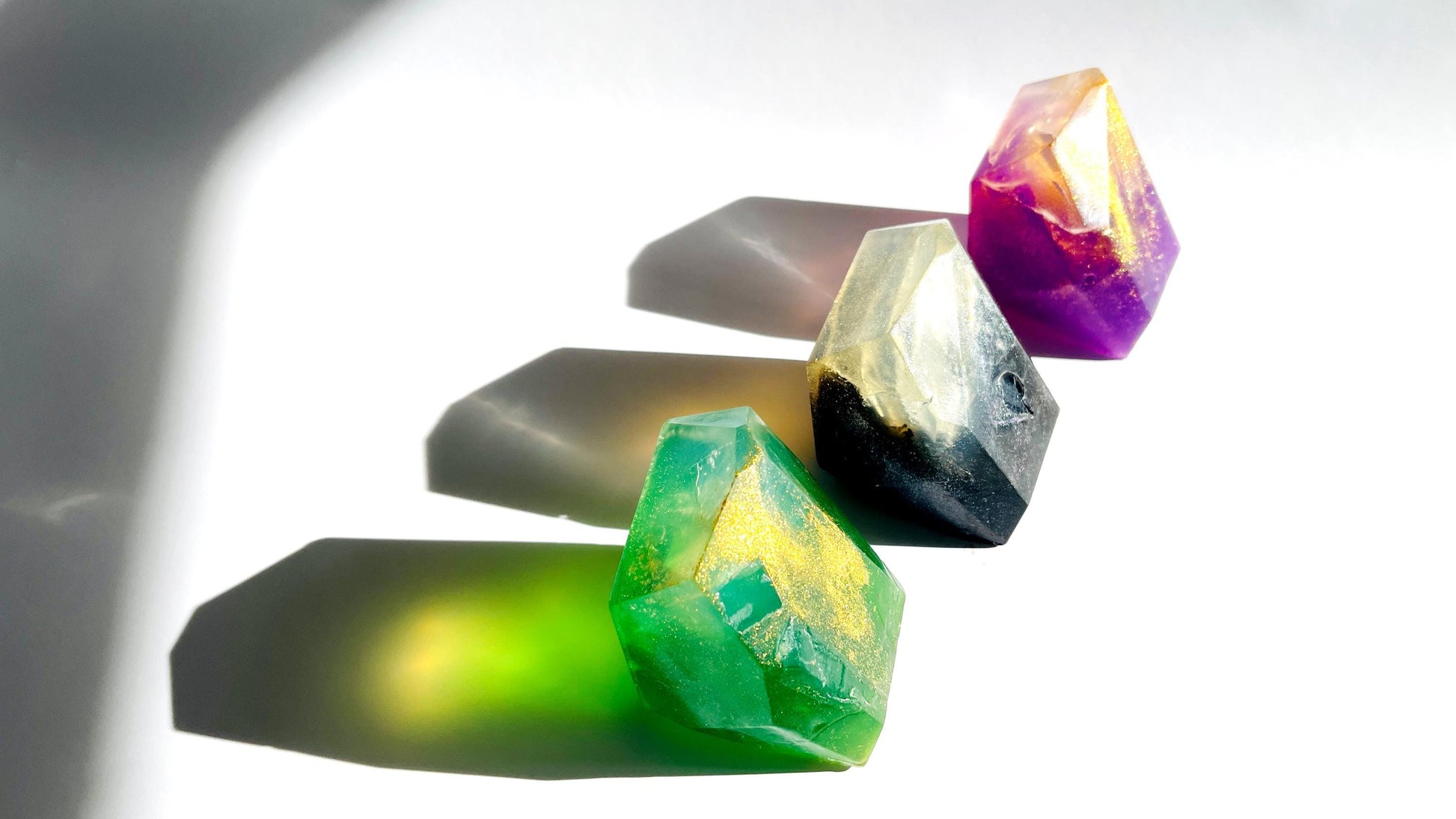 3 Colorful crystal gem shaped soaps on a reflective surface with a blurred background