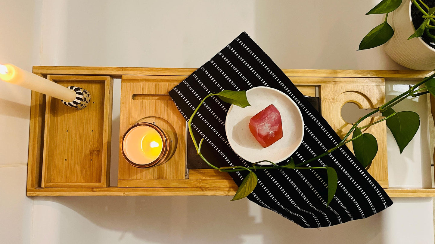 Wooden tray with a soap dish with a pink gem shaped soap, candle, and black striped towel.