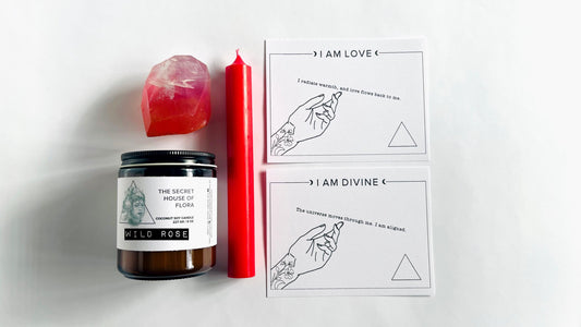 Pink taper candle, wild rose amber glass candle, pink crystal gem shaped soap, with affirmation cards on a white surface.