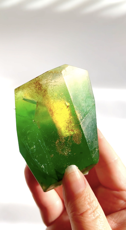 Green crystal gem shaped soap held in a hand against a white background