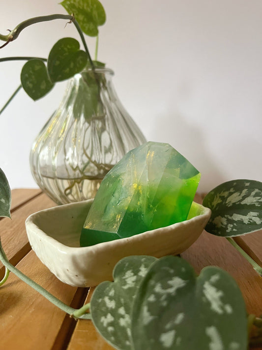 Green gem shape soap in a white dish with a plant in the background