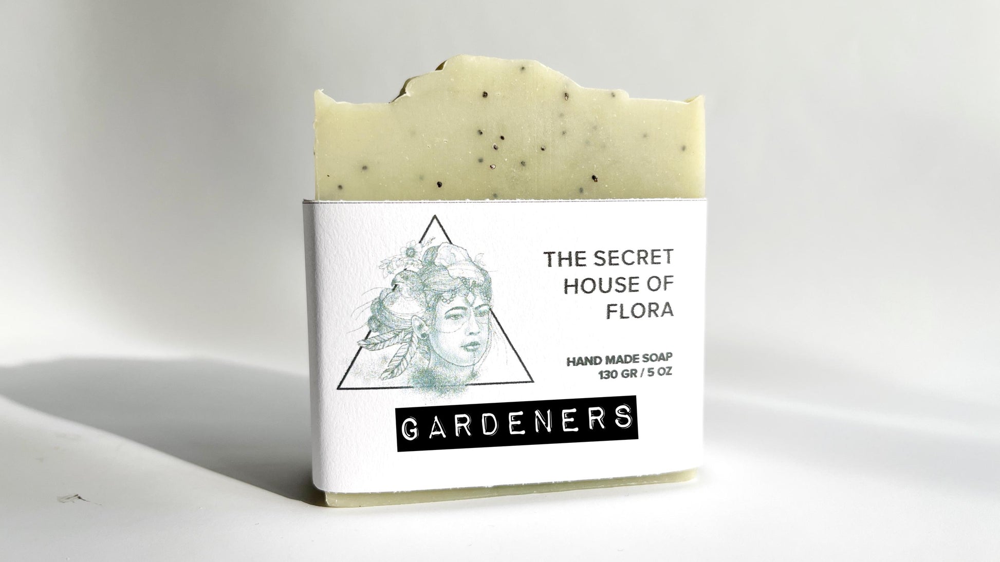 Bar of soap light green soap with poppy seeds sprinkled throughout, with a label on a white background.