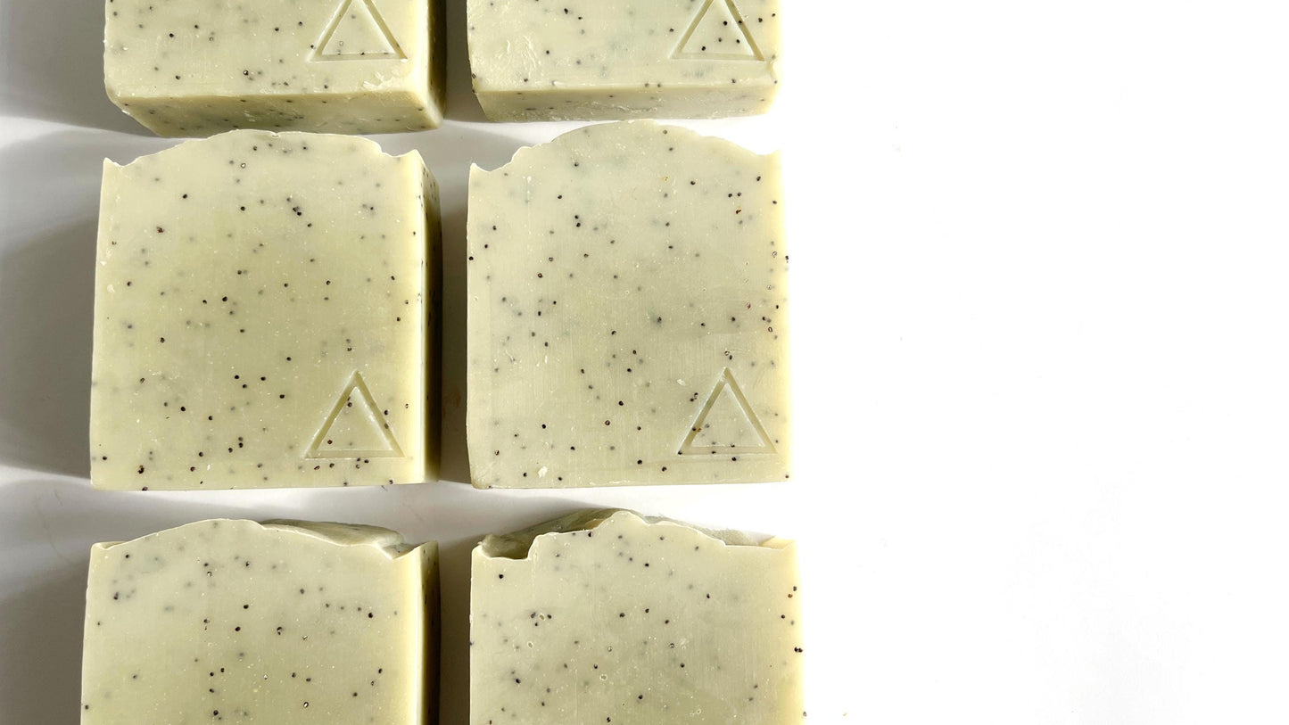 Six square bars of light green soap with a hand stamped triangle logo on each one, on a white background.