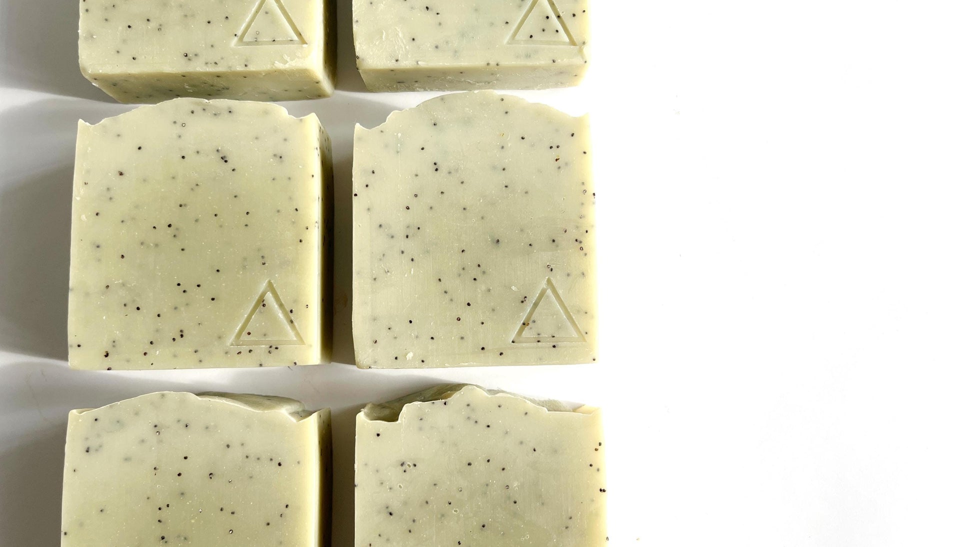 Six square bars of light green soap with a hand stamped triangle logo on each one, on a white background.