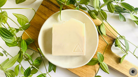 White bar of soap with light purple swirls on a white soap dish with green leaves around