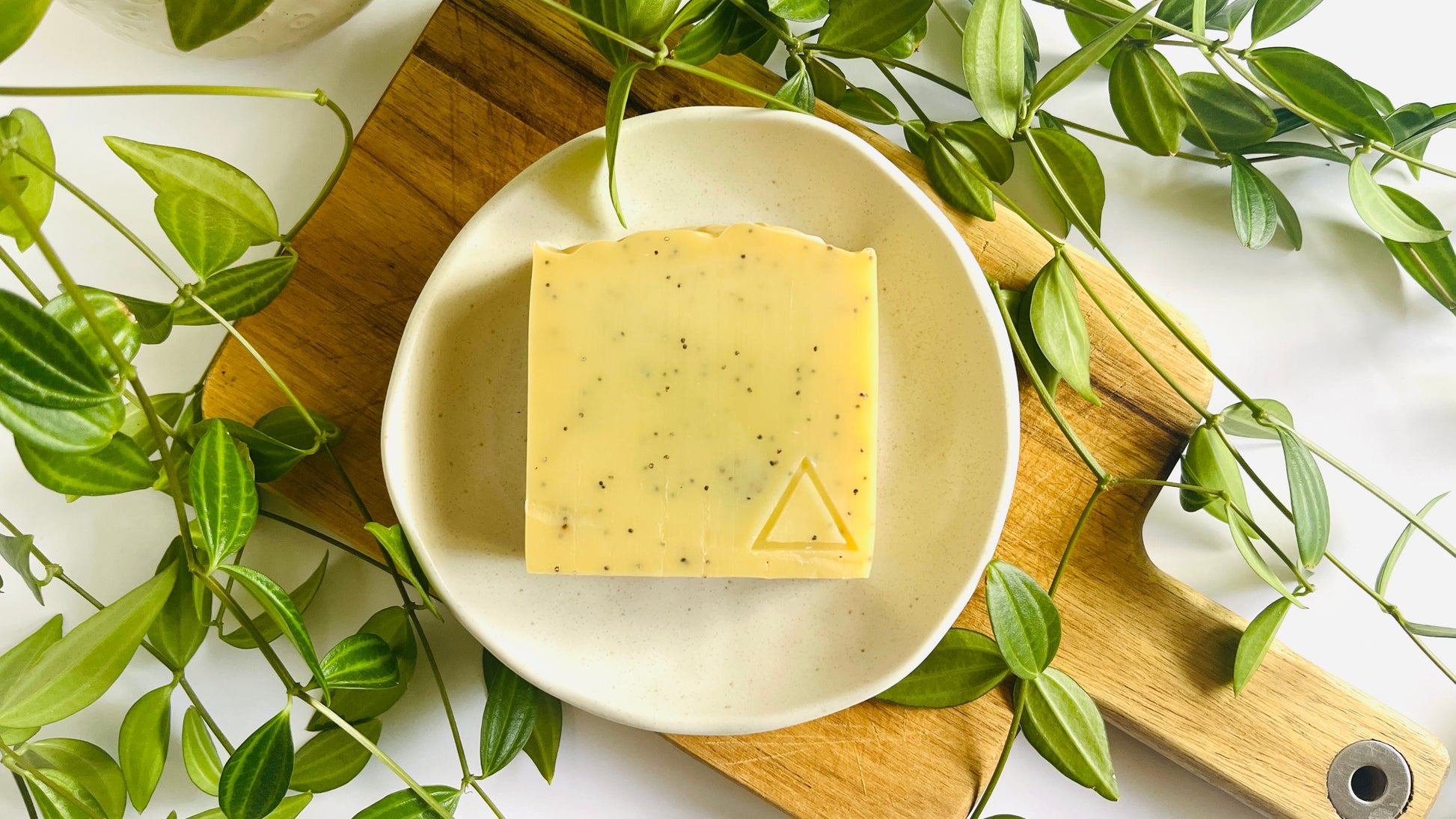 Bar of light yellow soap on a white soap dish with green leaves around