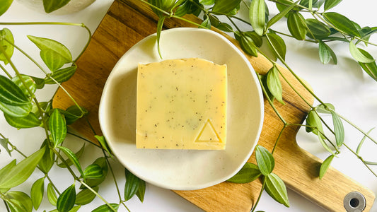 Bar of light yellow soap on a white soap dish with green leaves around