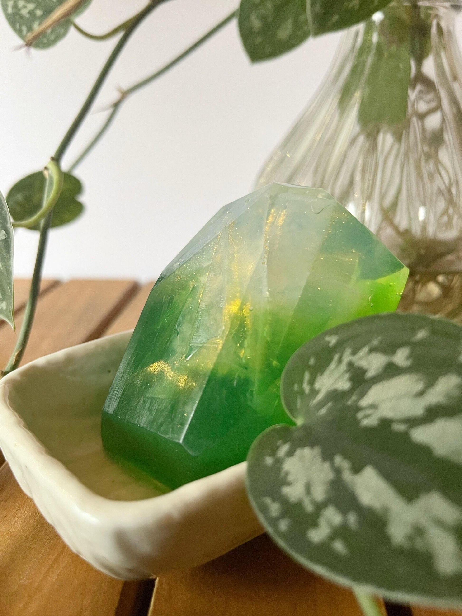 Green gem shaped soap bar in a white dish with a plant in the background