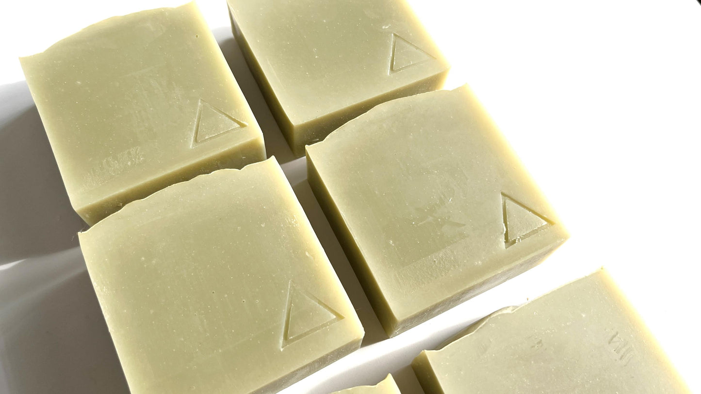 Five square bars of sage green soap with a triangle logo hand stamped into them on a white background.