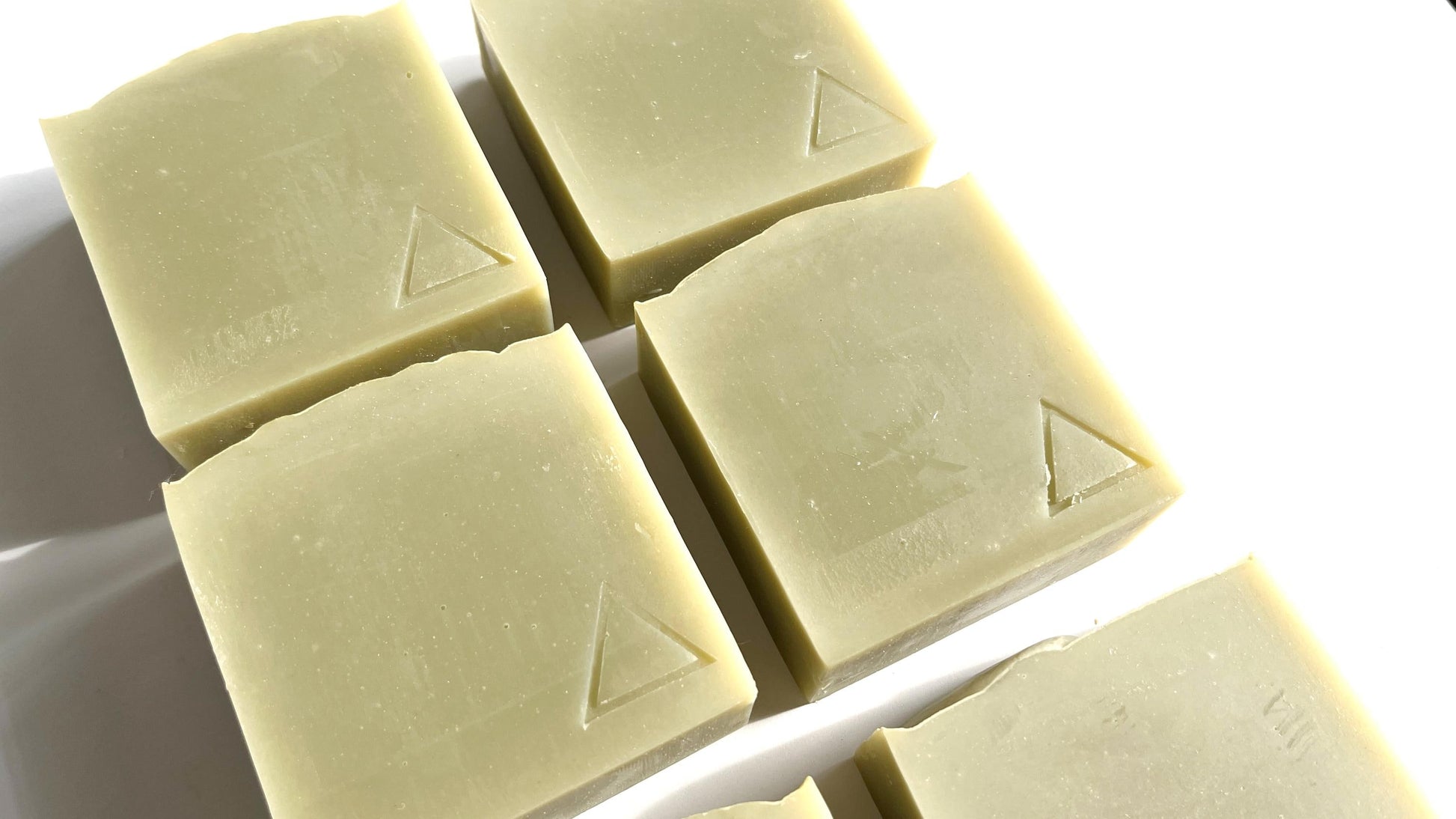 Five square bars of sage green soap with a triangle logo hand stamped into them on a white background.
