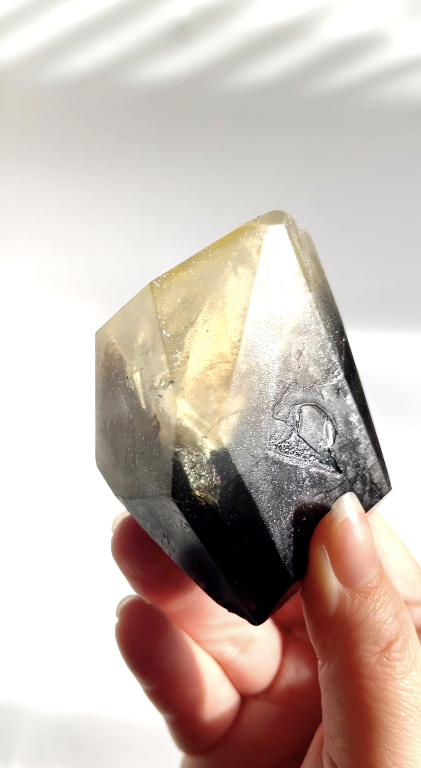 Person holding a smoky black with silver sparkle gem shaped soap against a white background