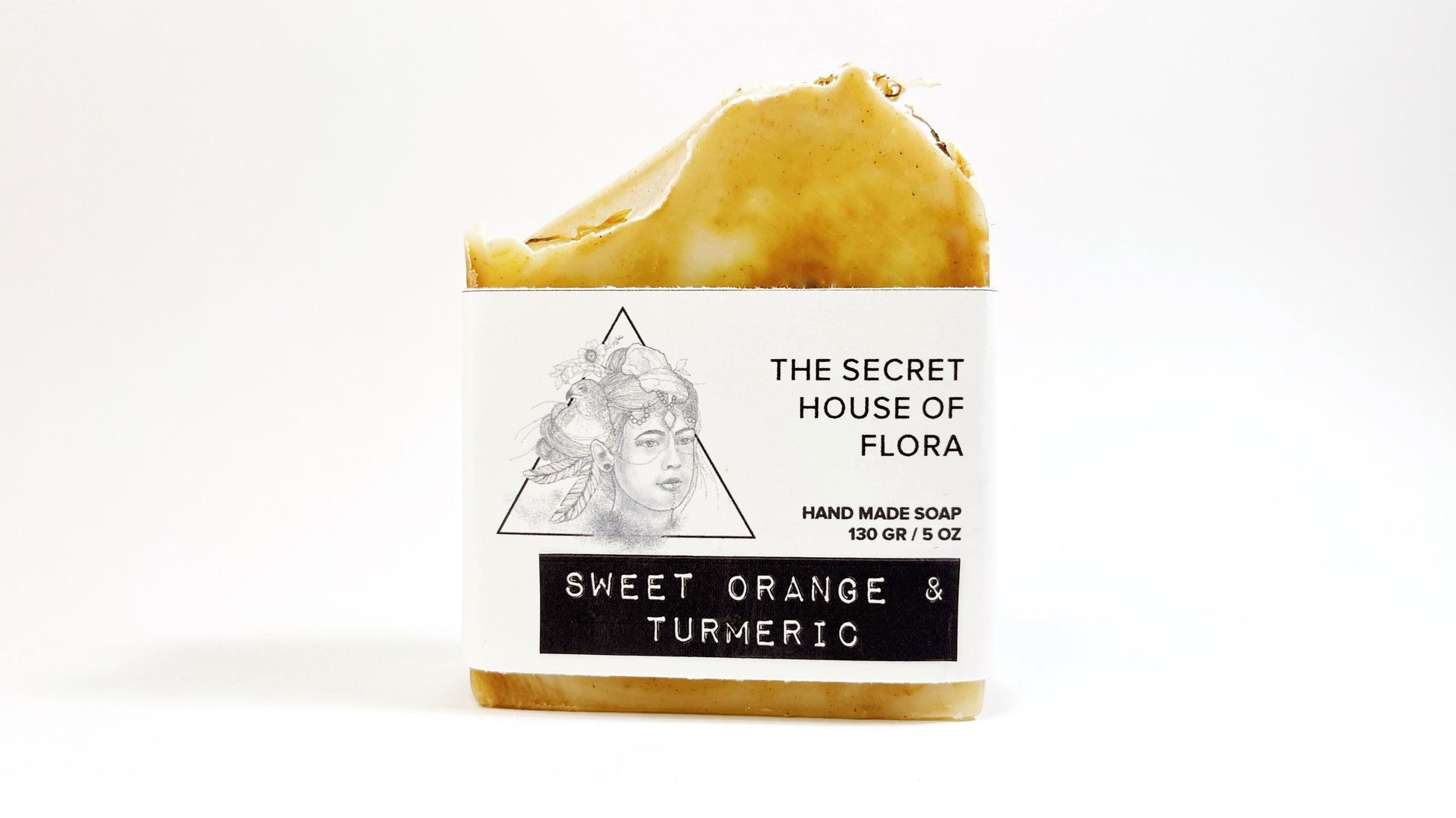 Bar of soap with beautiful orange and white swirls with packaging labeled 'The Secret House of Flora' on a white background.