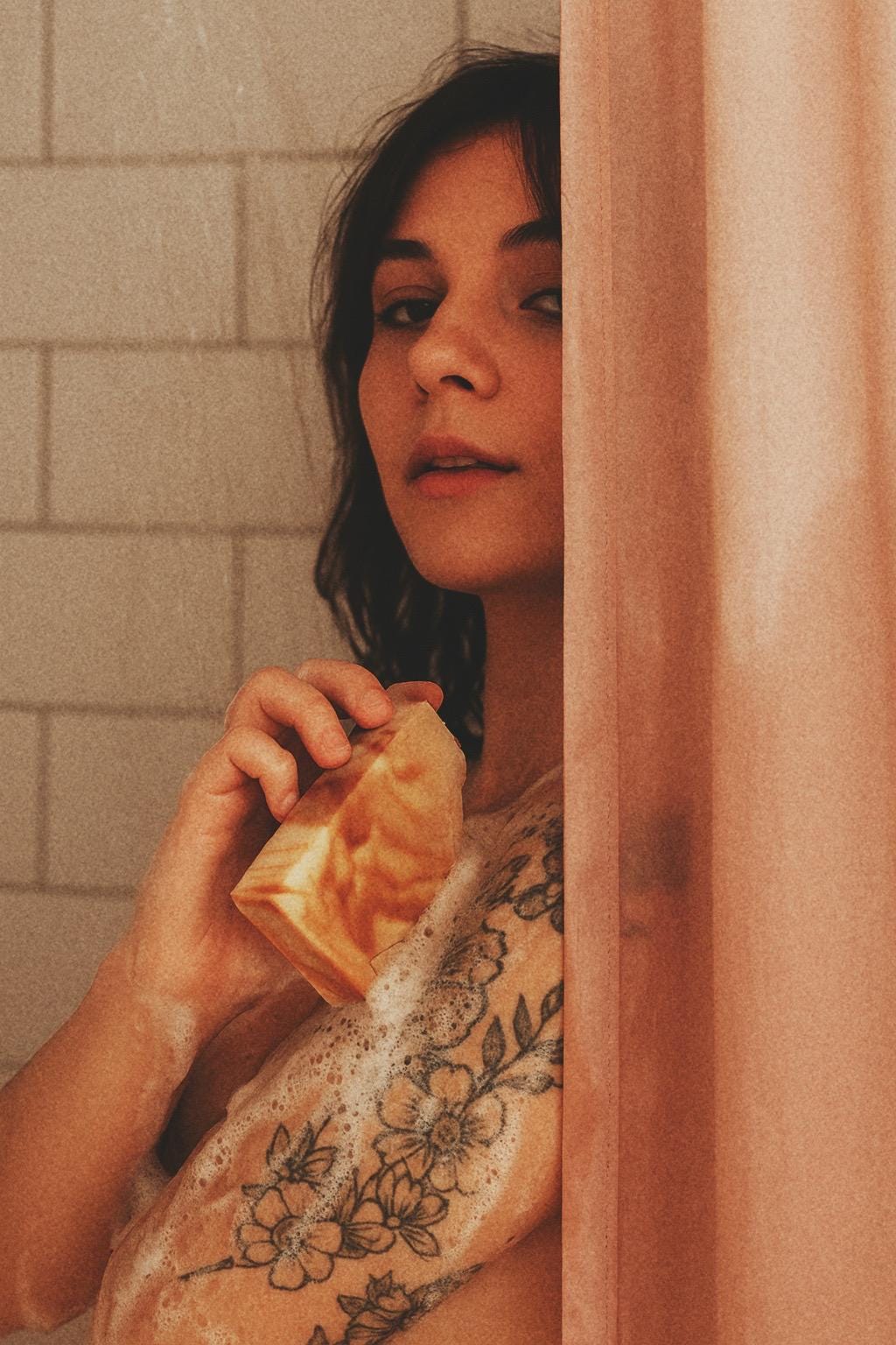 Woman holding an orange and white marbled bar of soap in a bathroom with tiled walls.