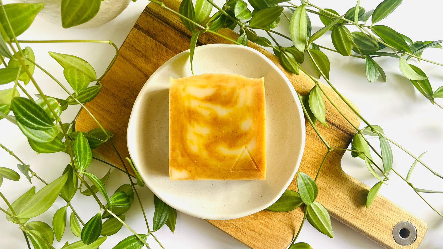 Bar of soap with beautiful orange and white swirls on a white soap dish with green leaves around.