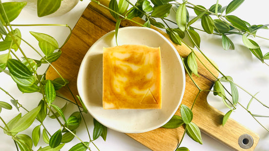 Bar of soap with beautiful orange and white swirls on a white soap dish with green leaves around.