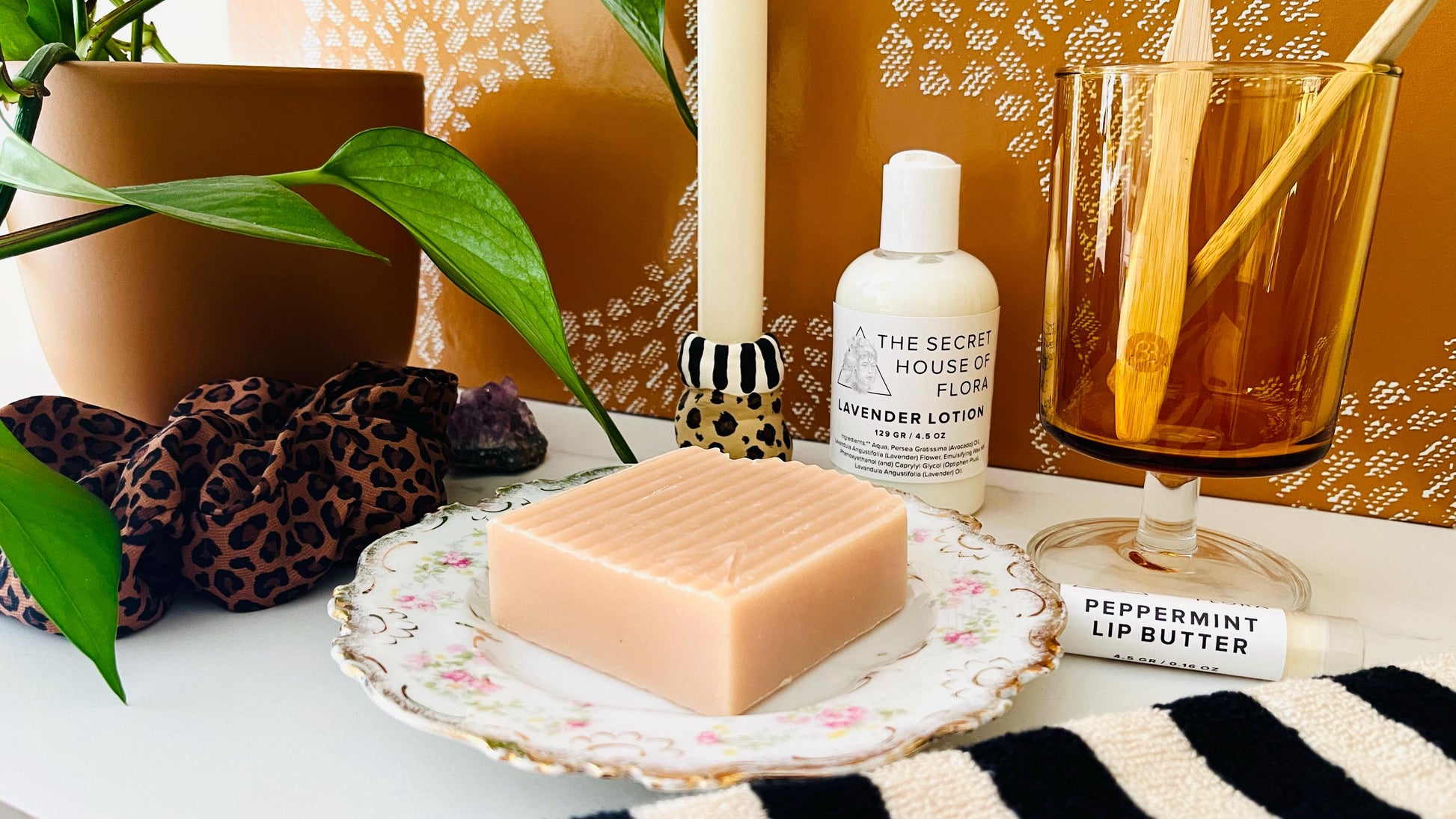 Bathroom counter scene with pink textured soap on a vintage floral soap dish, lotion bottle, with other items around.