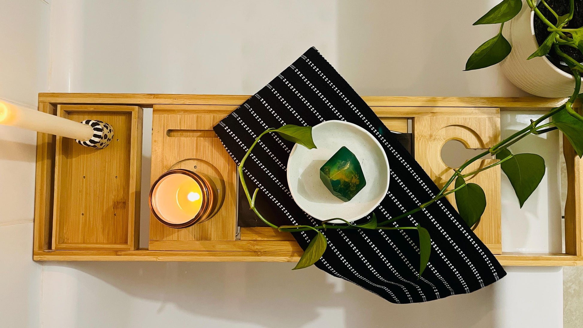 Decorative wooden tray with candle, and  gem shaped soap on a black and white striped towel.