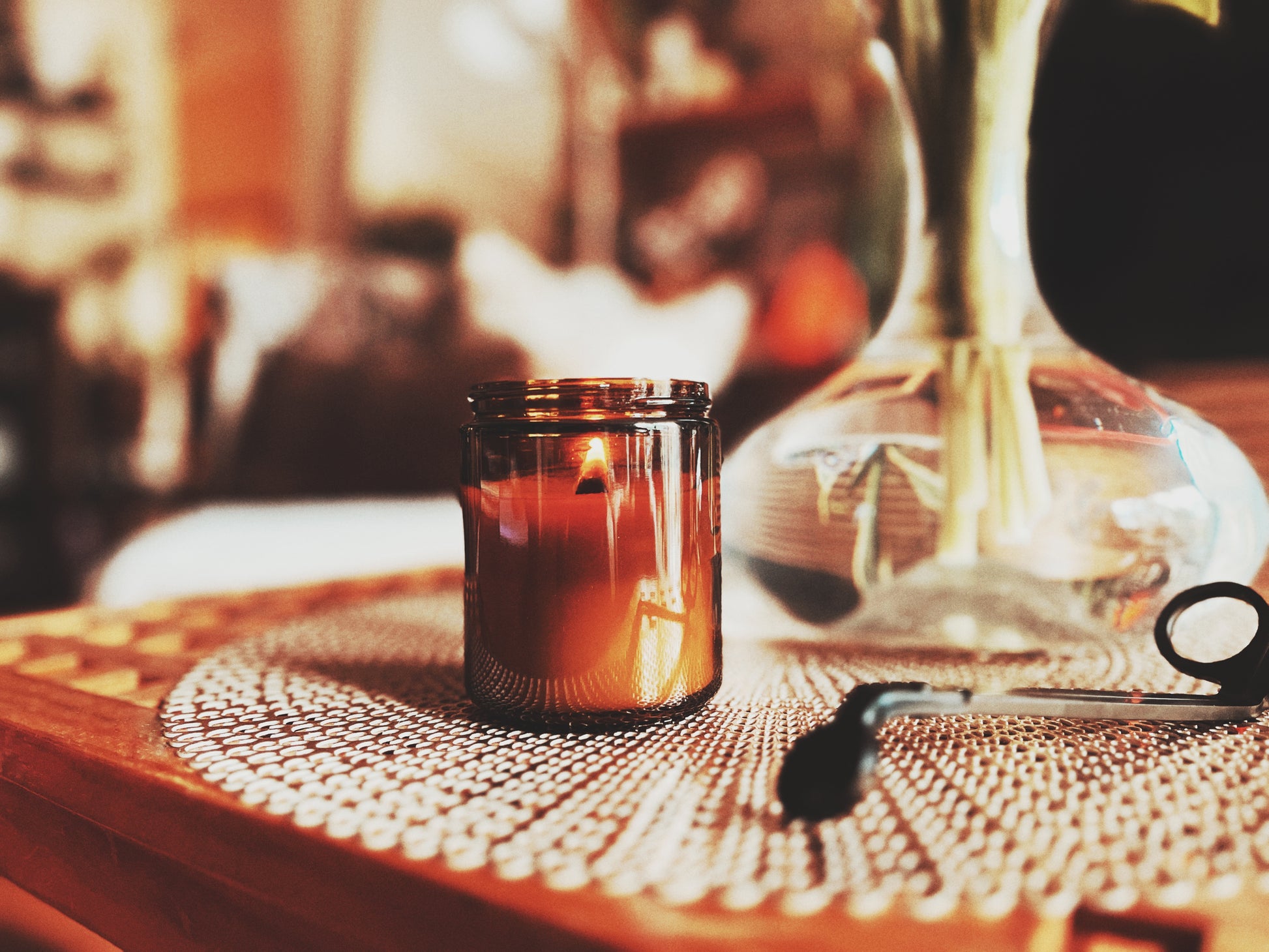 Candle in an amber glass jar on a textured surface with a blurred background.
